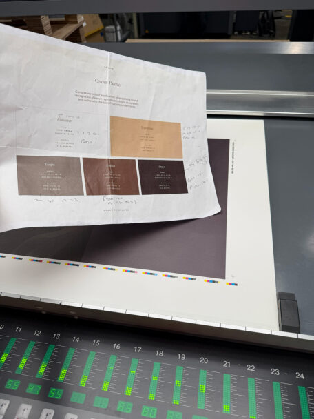 Brand colour palette proof held over a printing press control panel
